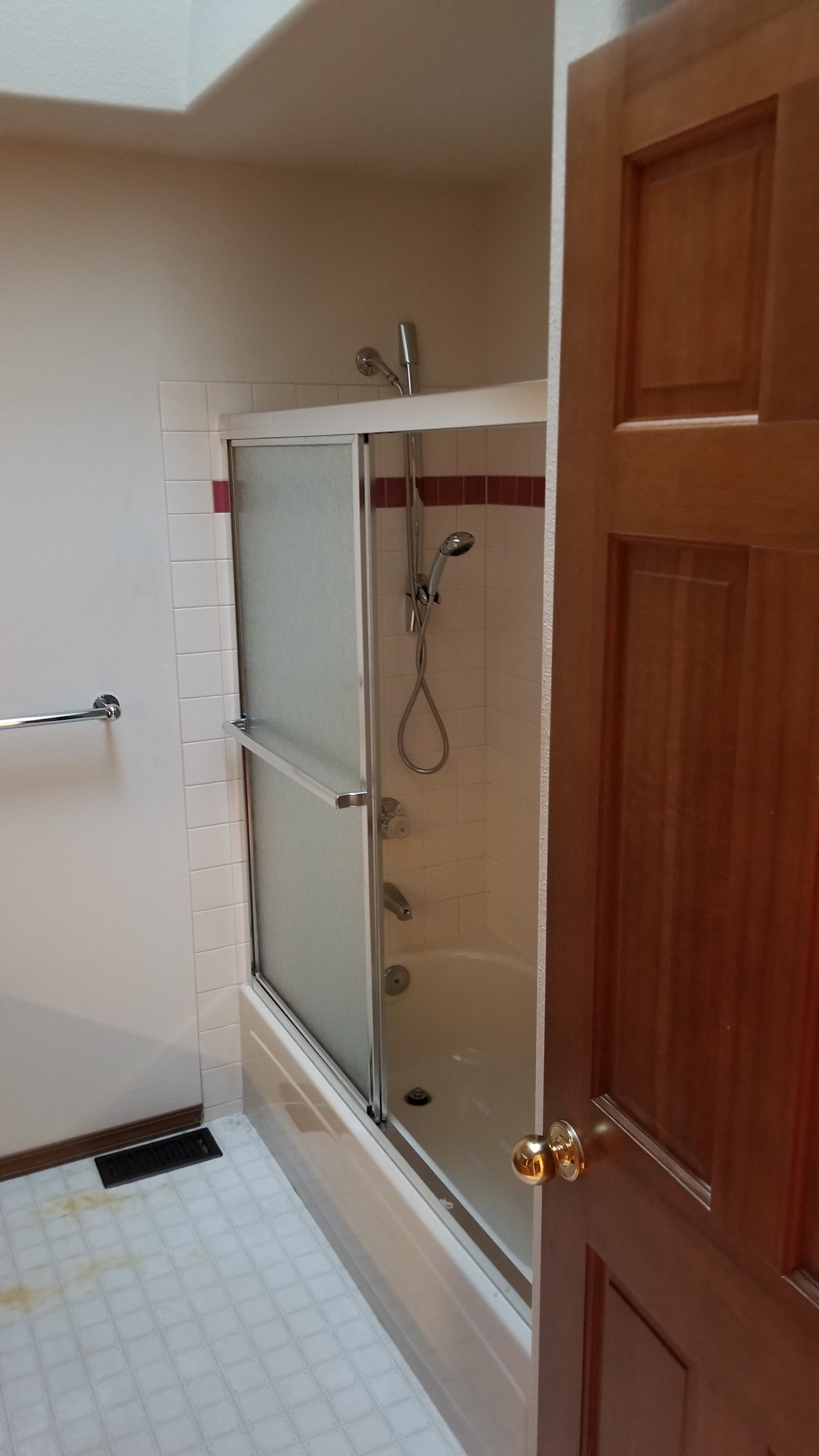 Secondary bathroom before remodel with a dated tub and shower combination, frosted sliding glass doors, white tile, and a maroon accent stripe