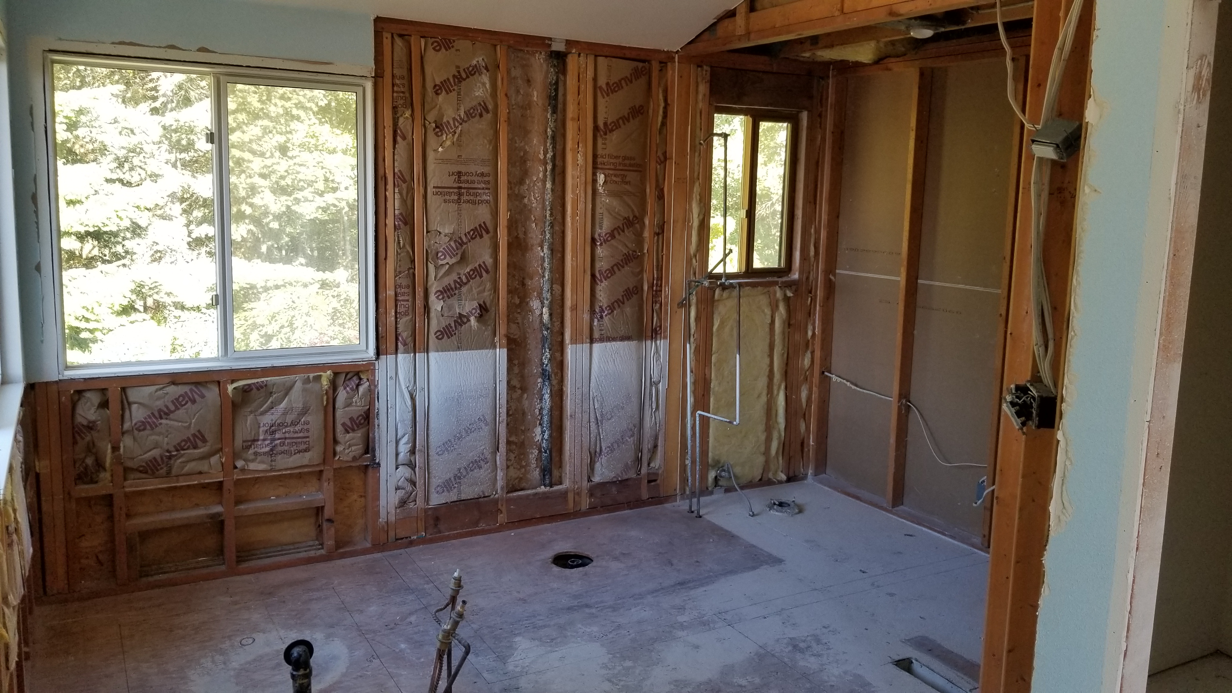 Home interior taken down to the studs during the Clyde Hill remodel, showing exposed wood framing, fiberglass insulation, and rough plumbing before reconstruction