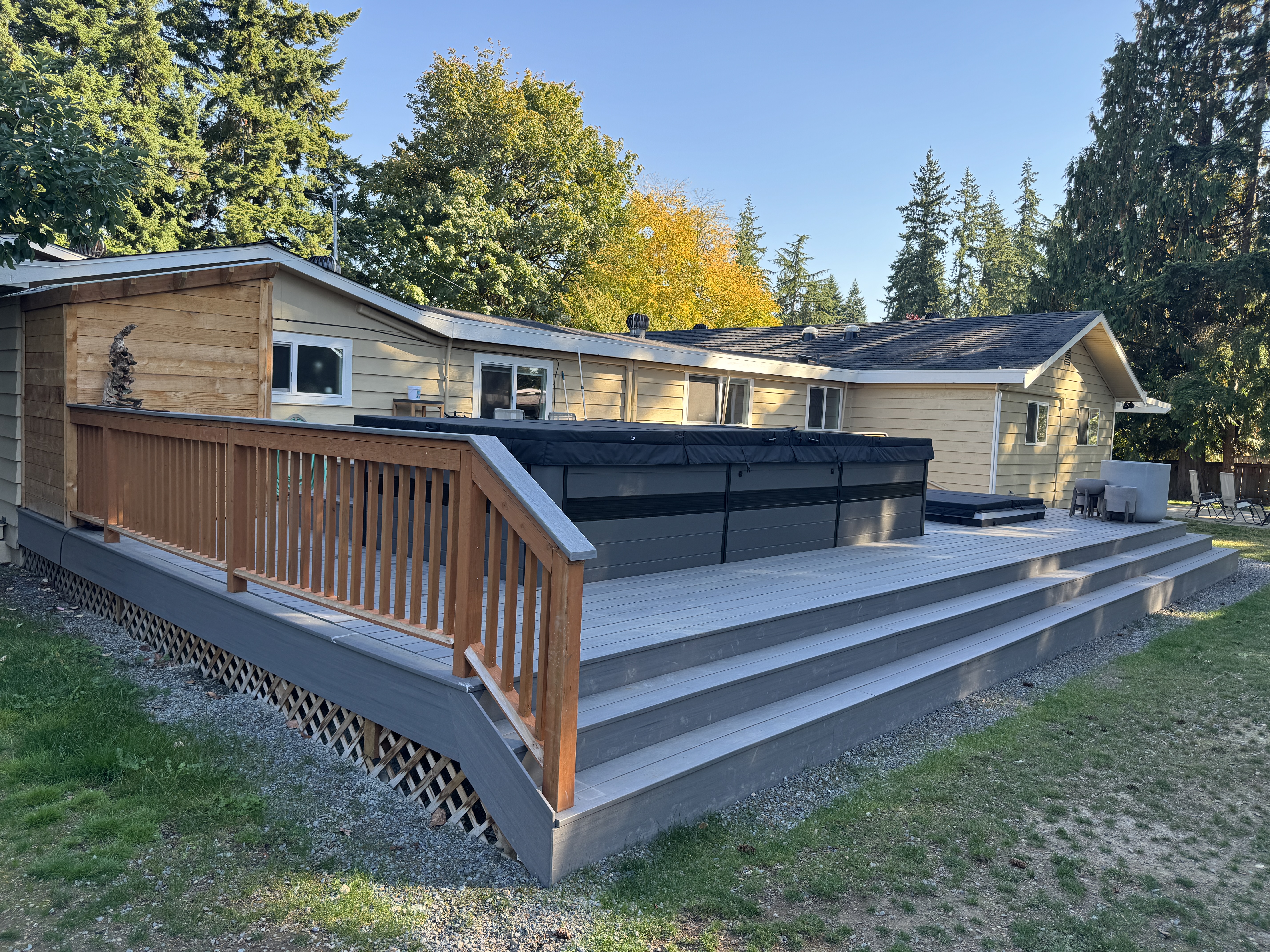 Finished composite deck at golden hour with cedar railing, lattice skirting and wide steps in Kenmore