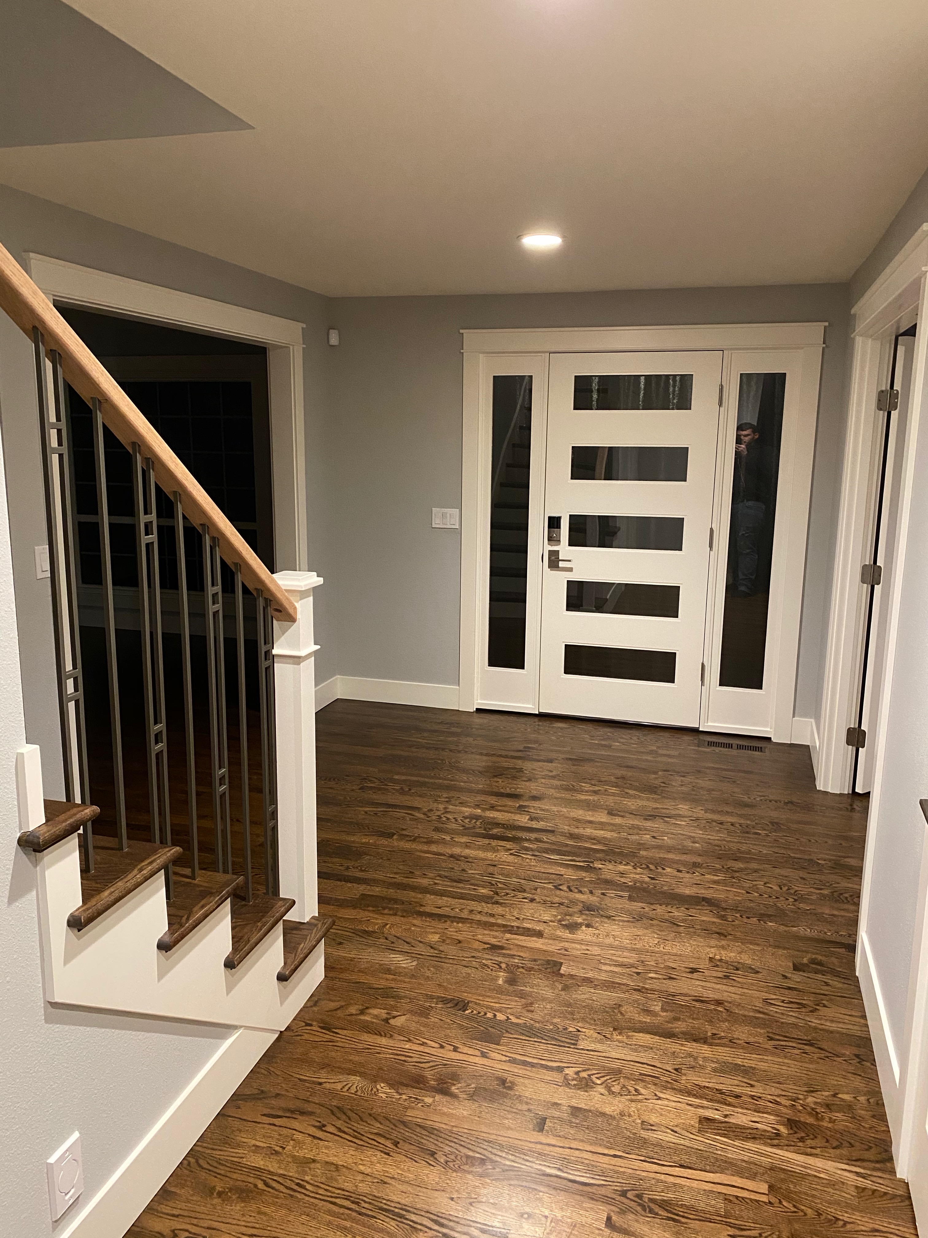 Remodeled entry foyer with a custom white modern front door featuring frosted glass panels and glass sidelights, warm hardwood floors, and a smart lock