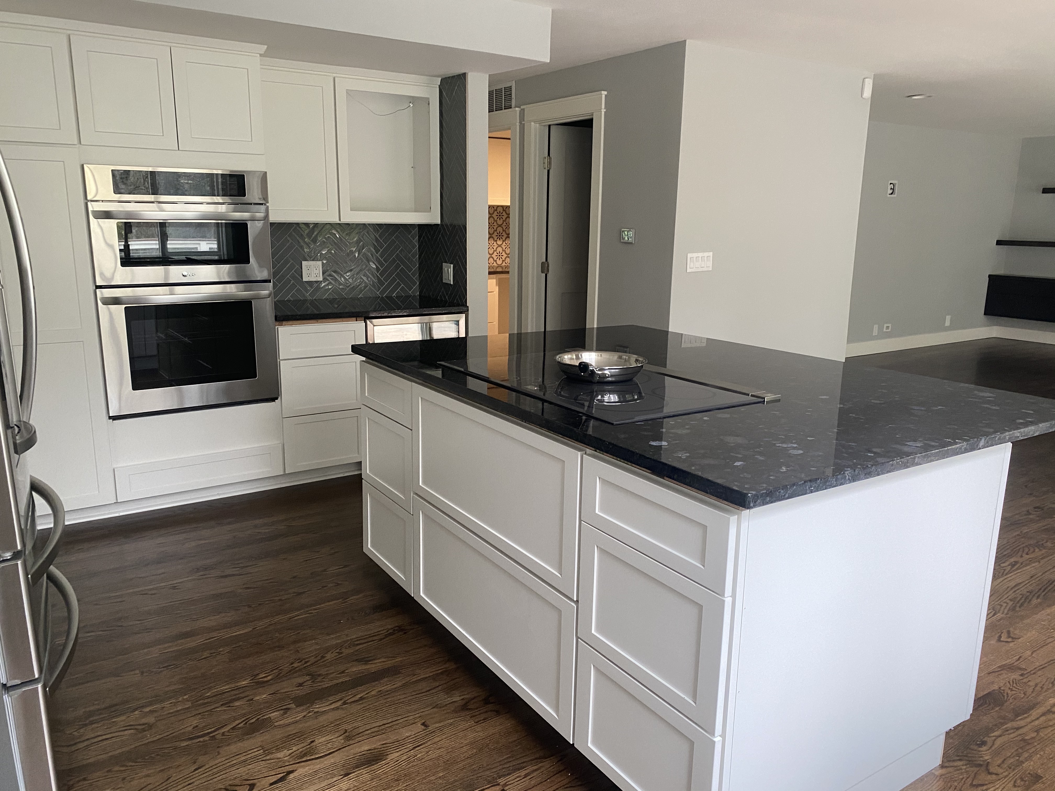 Remodeled luxury kitchen with white shaker cabinets, black pearl granite island with integrated cooktop, herringbone tile backsplash, and stainless steel LG refrigerator