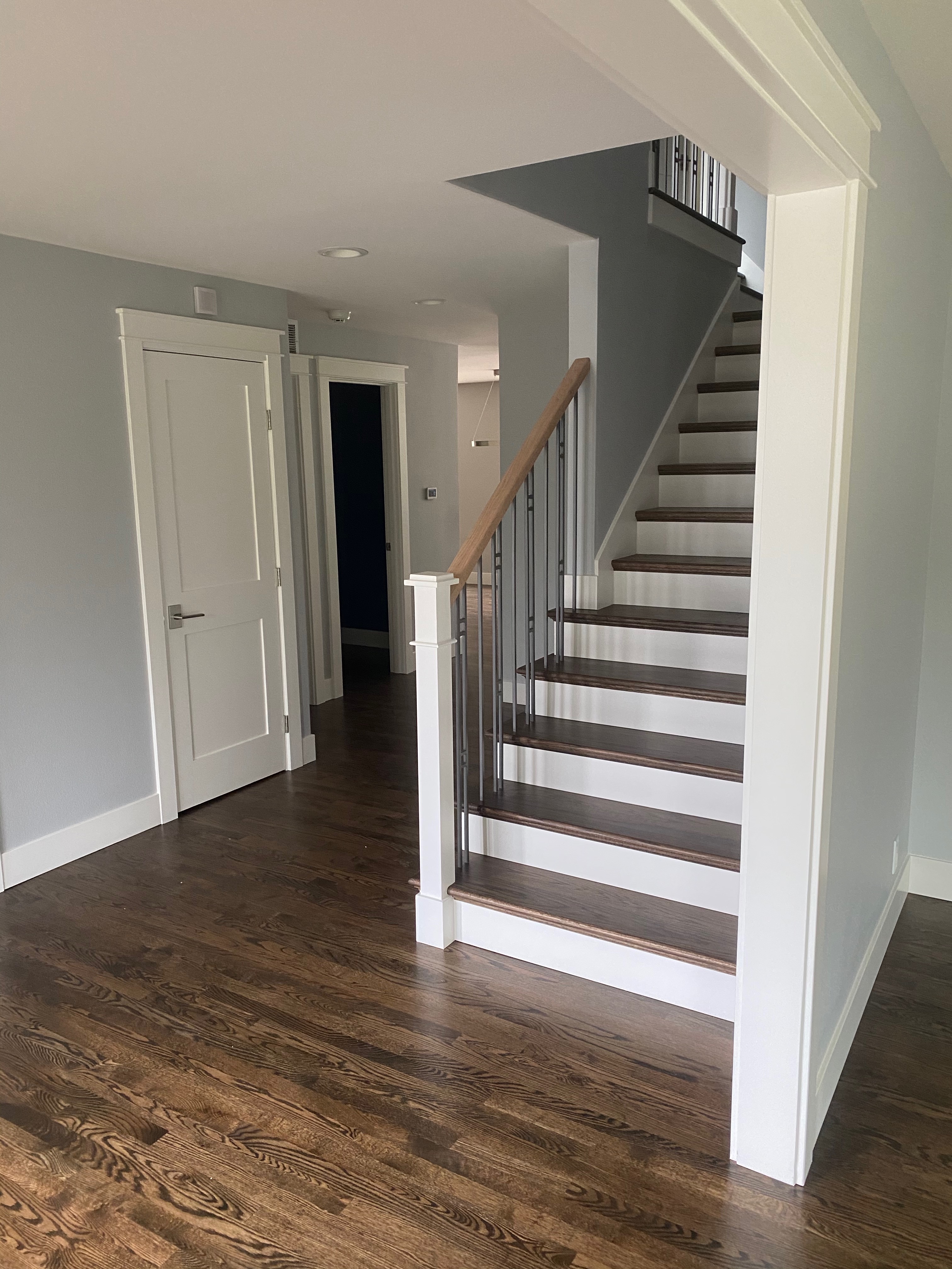 Custom remodeled staircase with stained hardwood treads, white painted risers, iron balusters, hardwood handrail, and dark walnut flooring