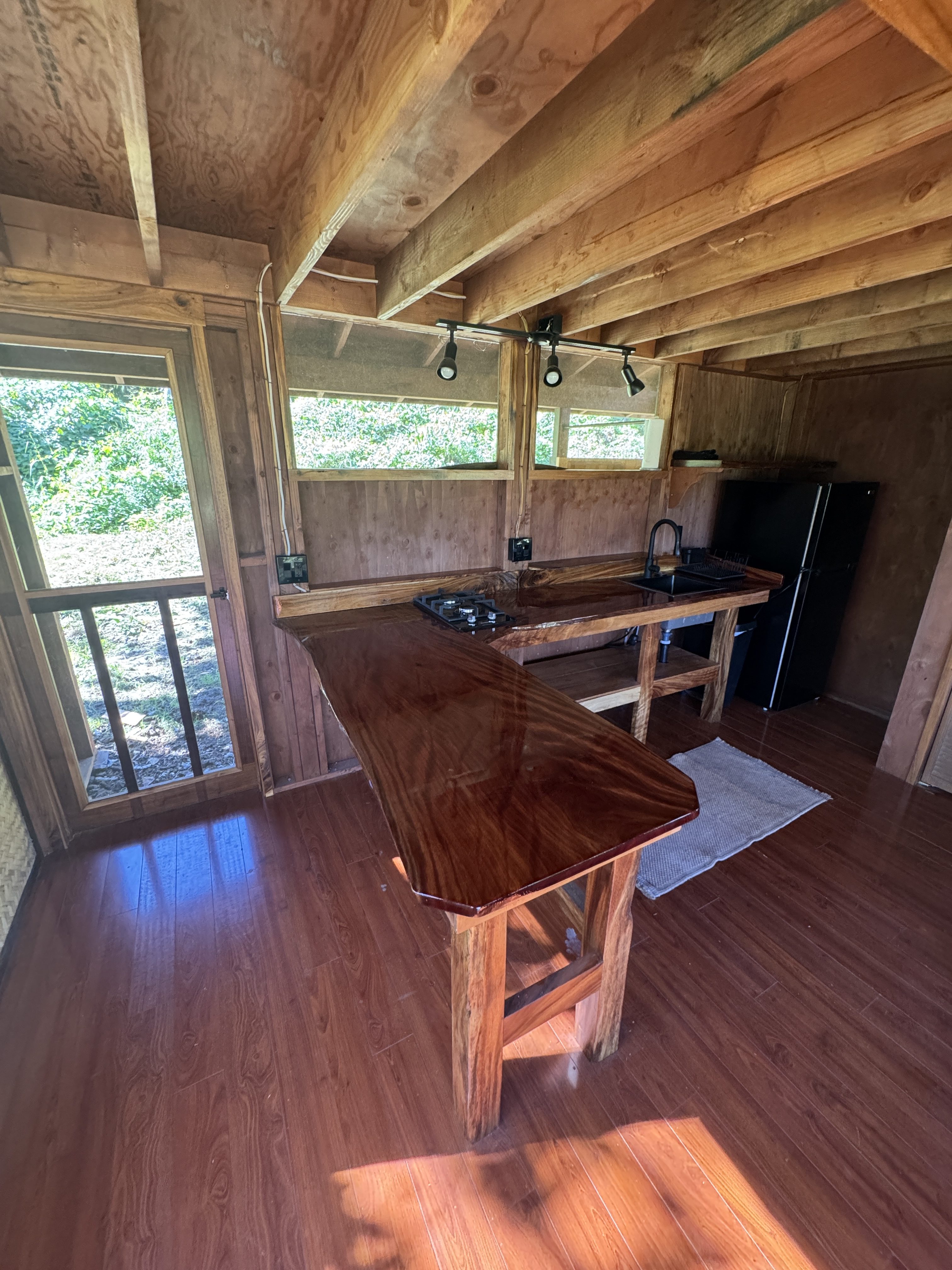 A cabin kitchen with a glass-smooth live-edge monkeypod counter, gas cooktop, sink and hardwood floors