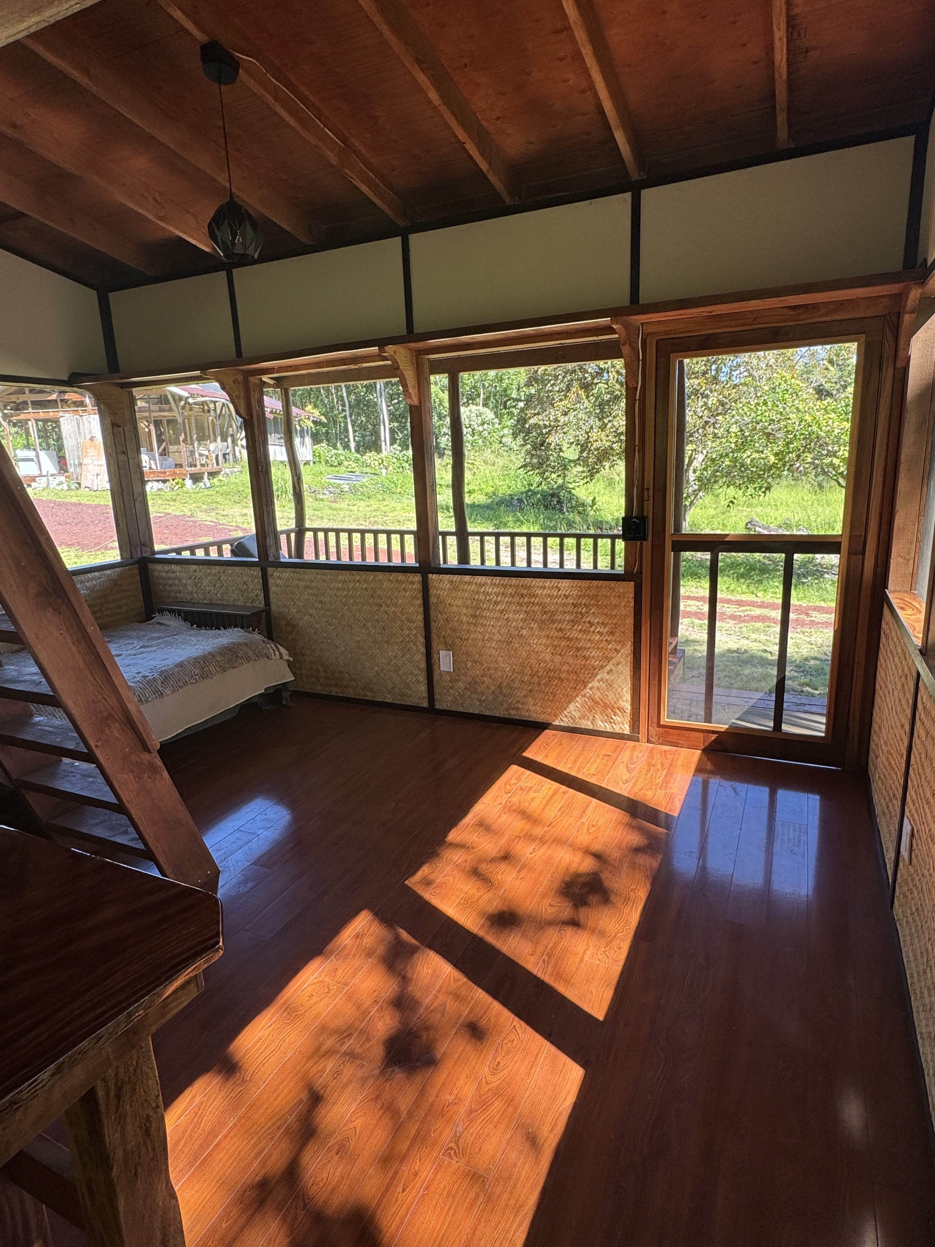 A screened interior room with woven lauhala wainscot, a polished hardwood floor, and a daybed by the windows