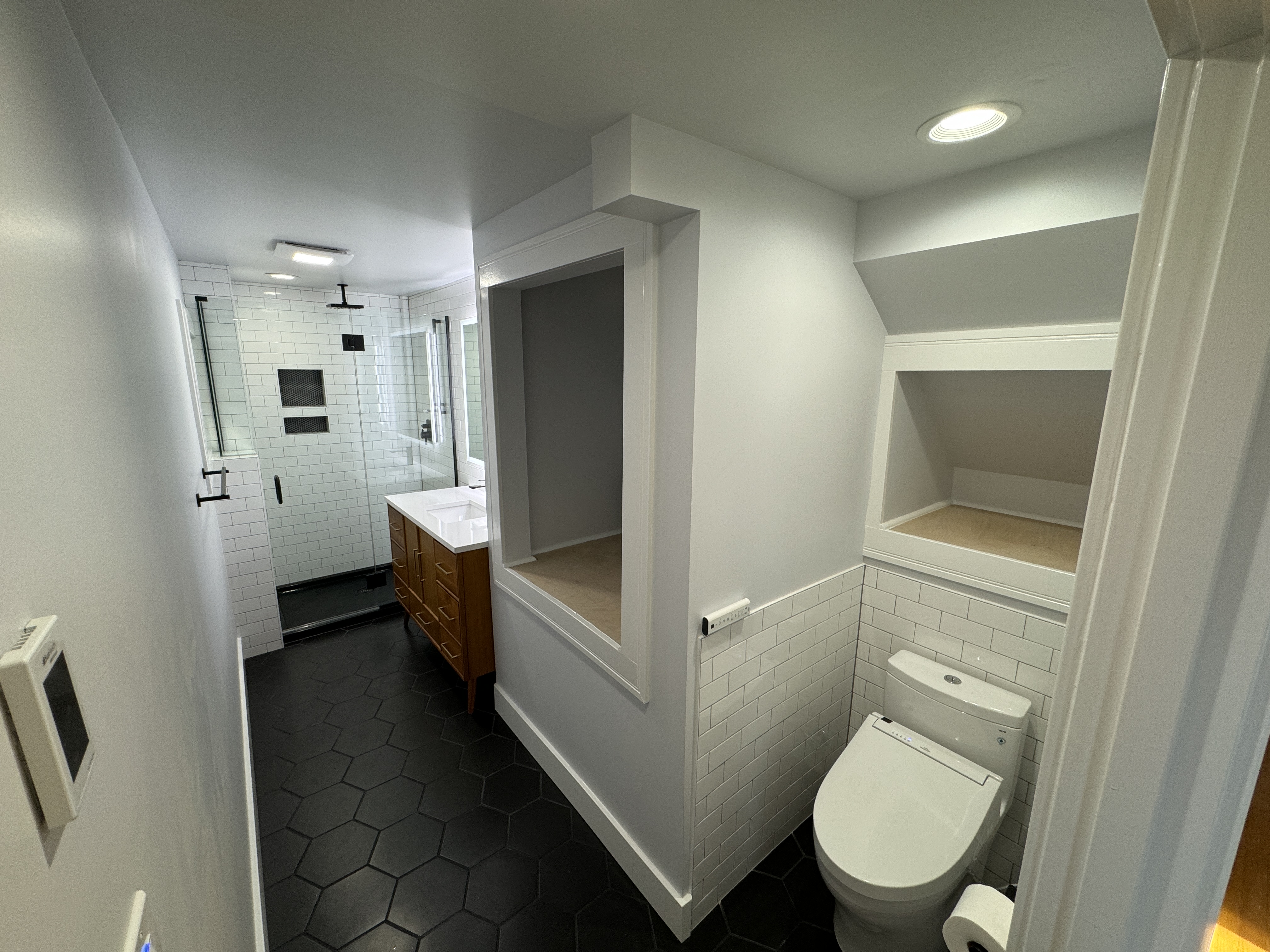 After: bright finished master bathroom with a recessed storage niche, vanity, and charcoal hexagon floor