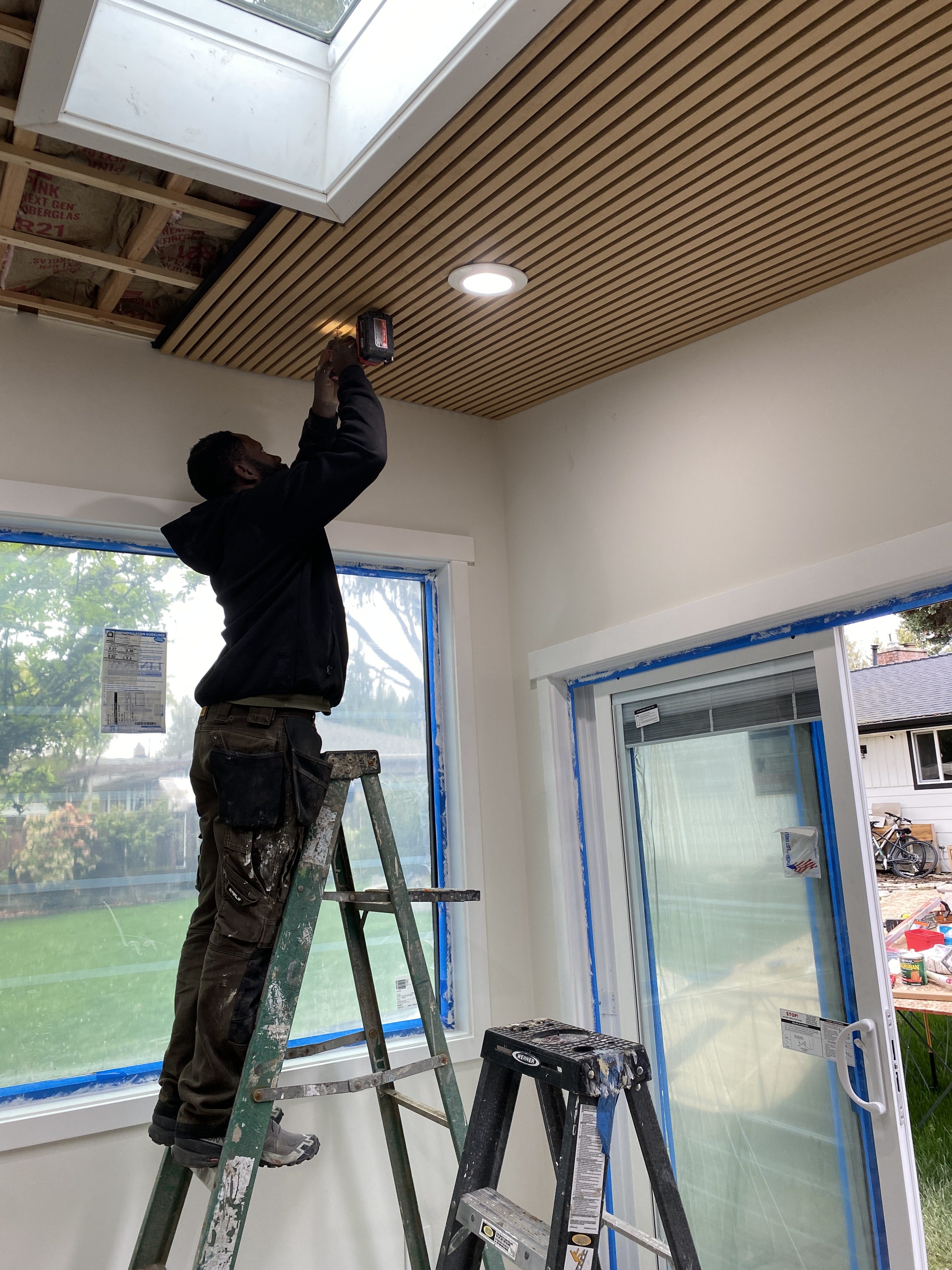 Interior finish underway with R-21 insulation, wood-slat acoustic ceiling installation, skylight well and recessed LED lighting
