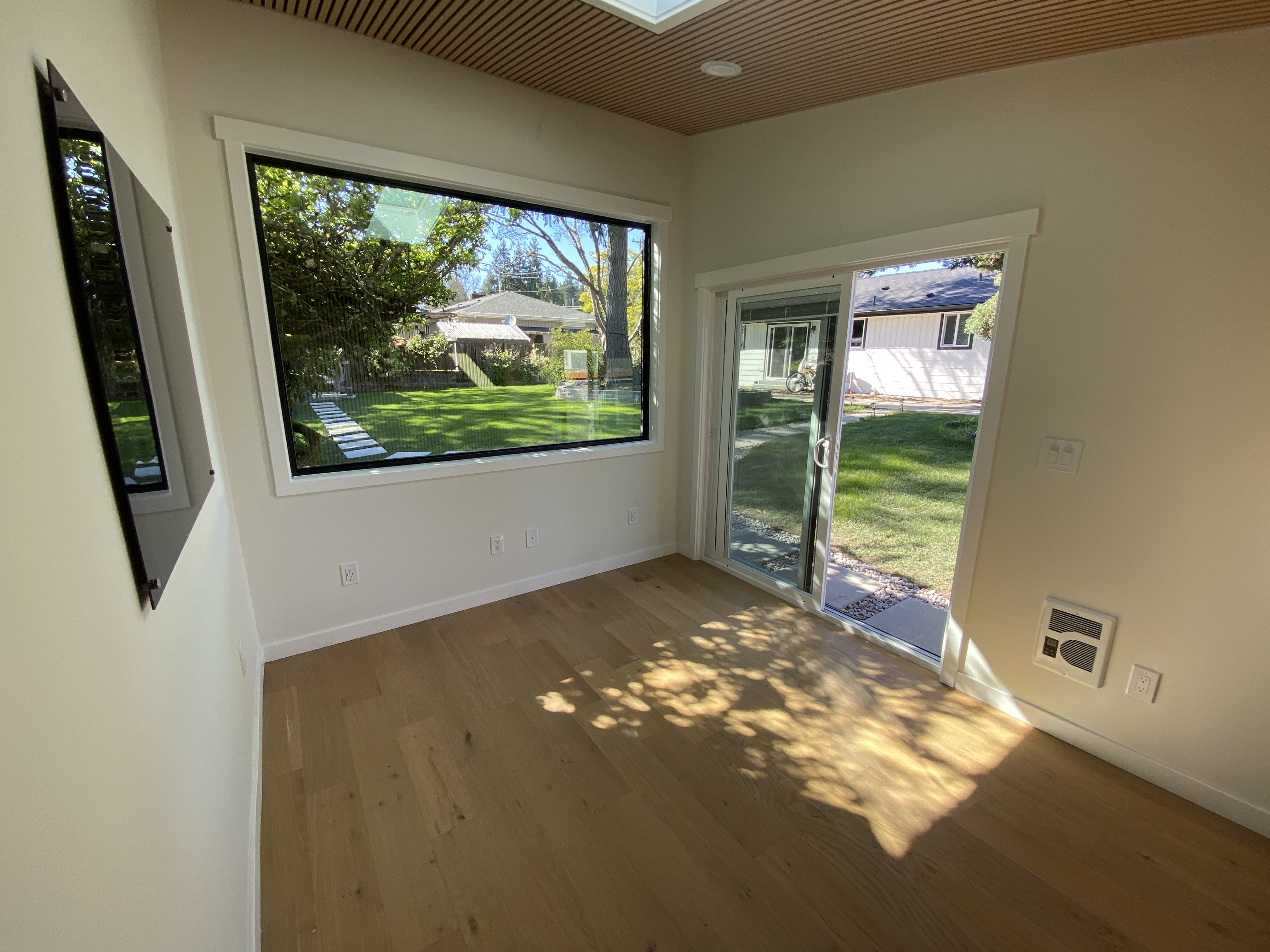Finished backyard office interior in Bothell with large black-framed picture window, sliding glass door, wood-slat ceiling and white oak floors