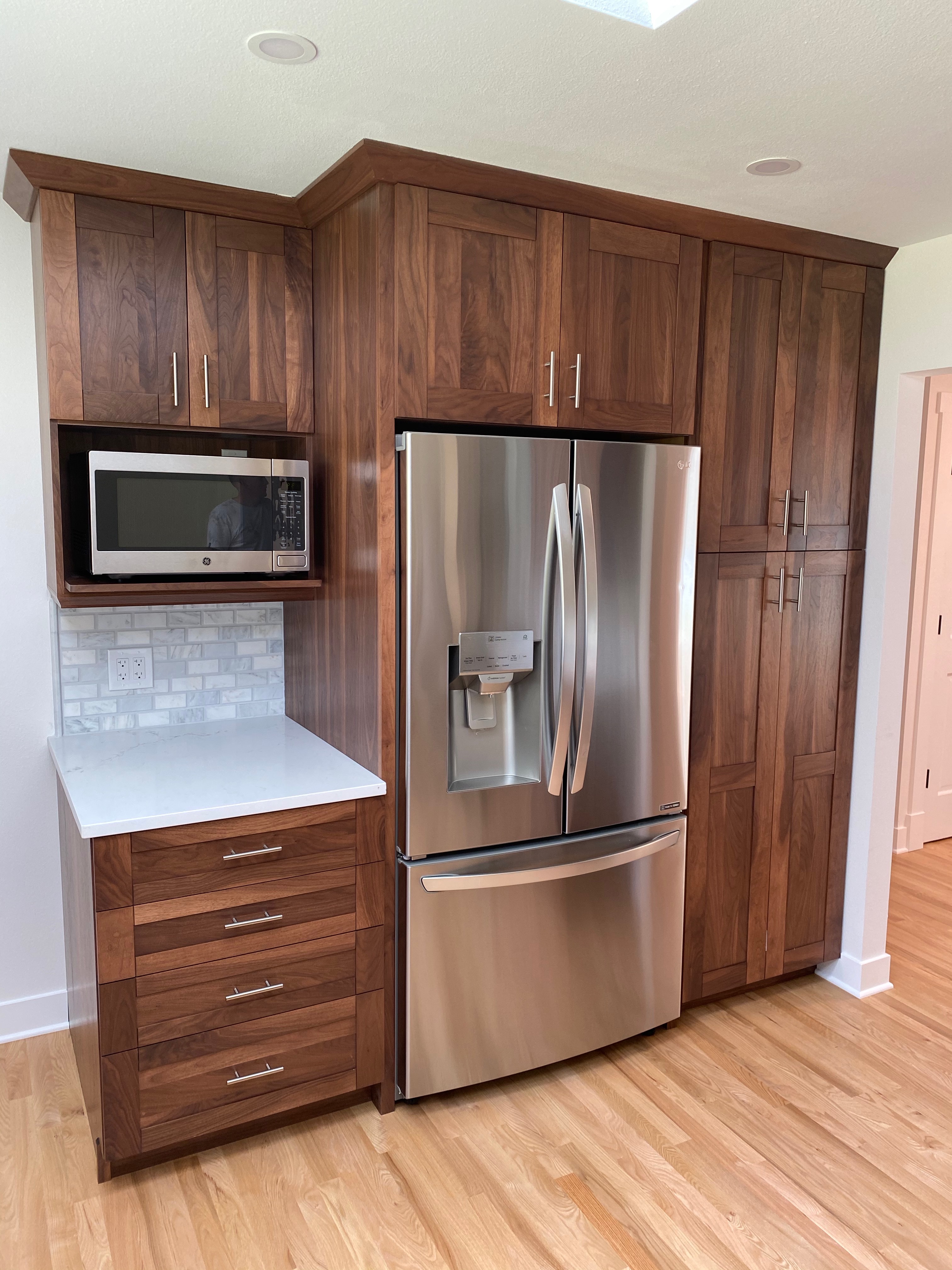 Detail of the finished Issaquah kitchen showing the full-height walnut pantry wall, integrated microwave nook, marble backsplash, and stainless French-door refrigerator