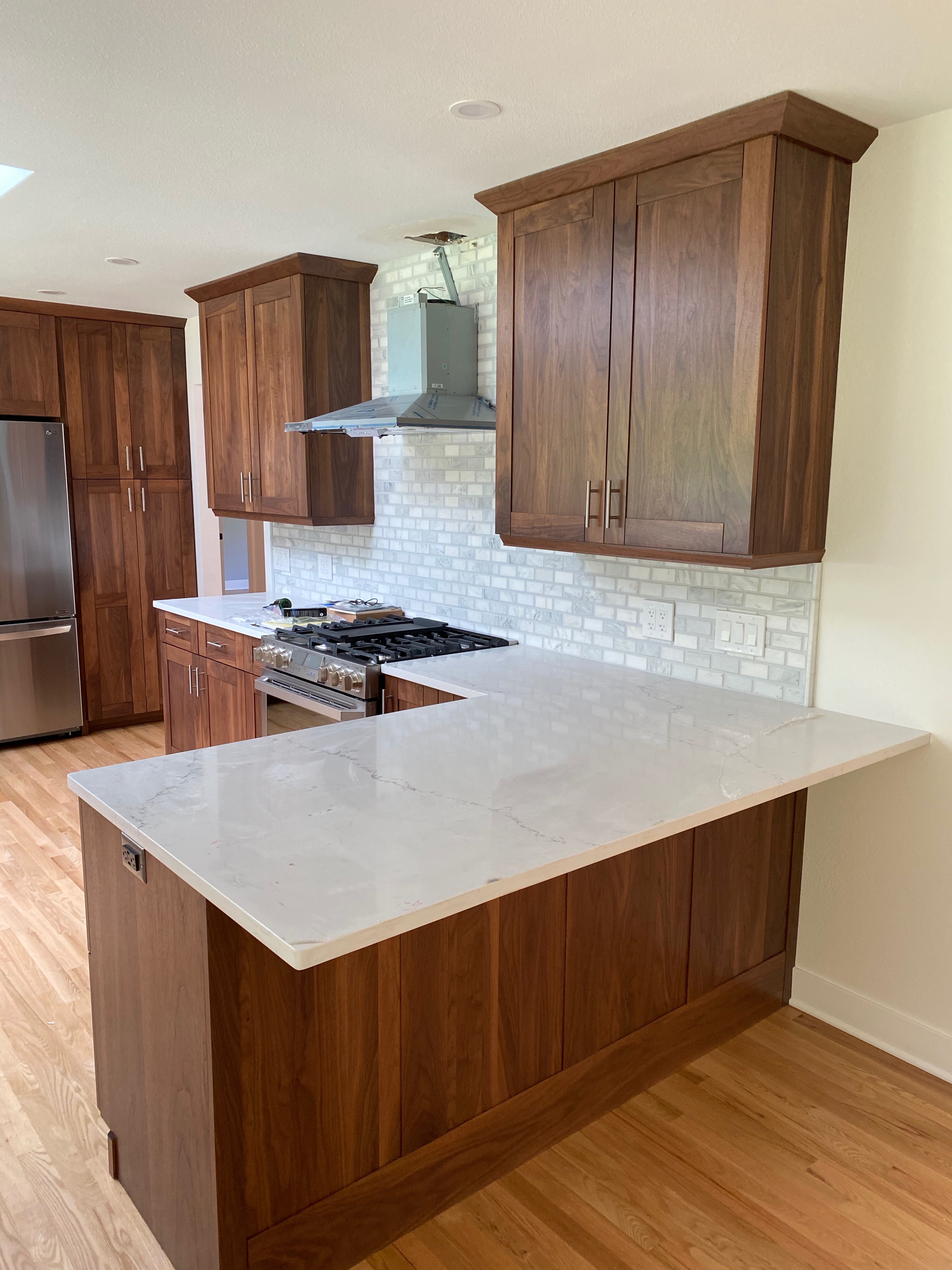 After photo of the completed Issaquah kitchen with a gas range, stainless hood, marble subway backsplash, walnut cabinets, and skylights filling the room with daylight