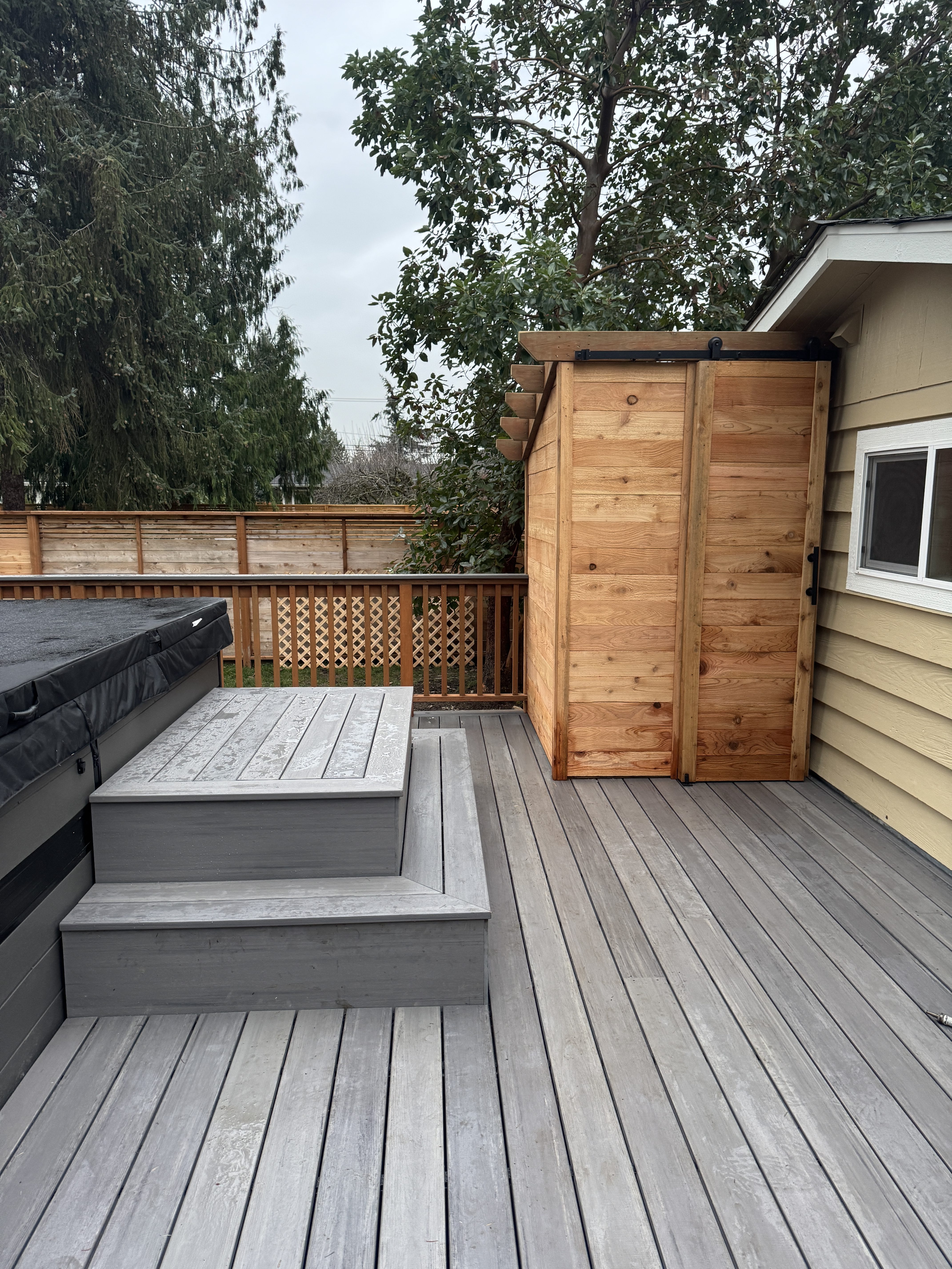 Enclosed cedar outdoor shower with sliding barn door and cedar privacy fence beside the deck in Kenmore WA