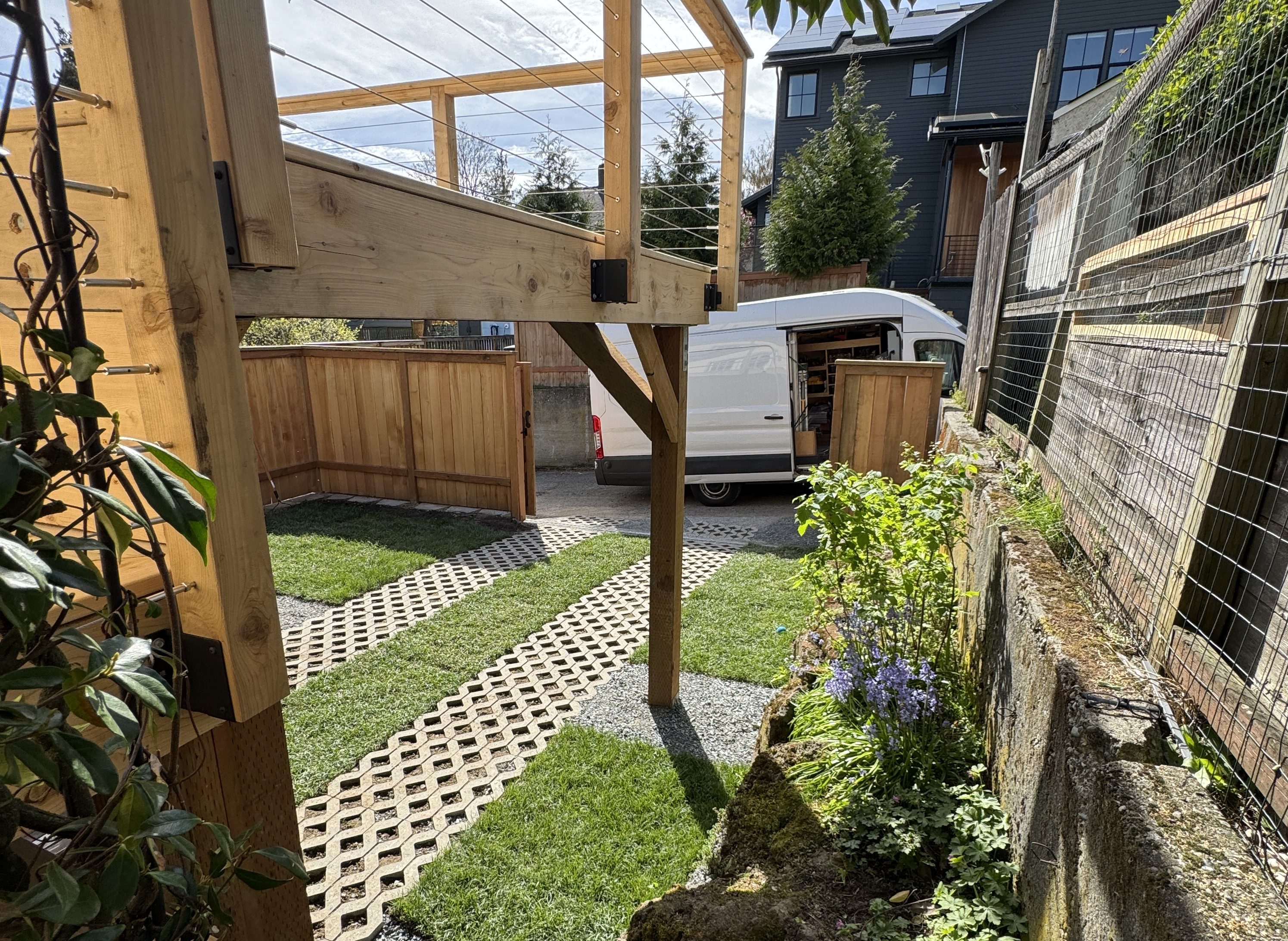 Permeable grass-paver driveway running between sod panels into a Woodinville backyard, with cedar privacy fence and sliding vehicle gate alongside.