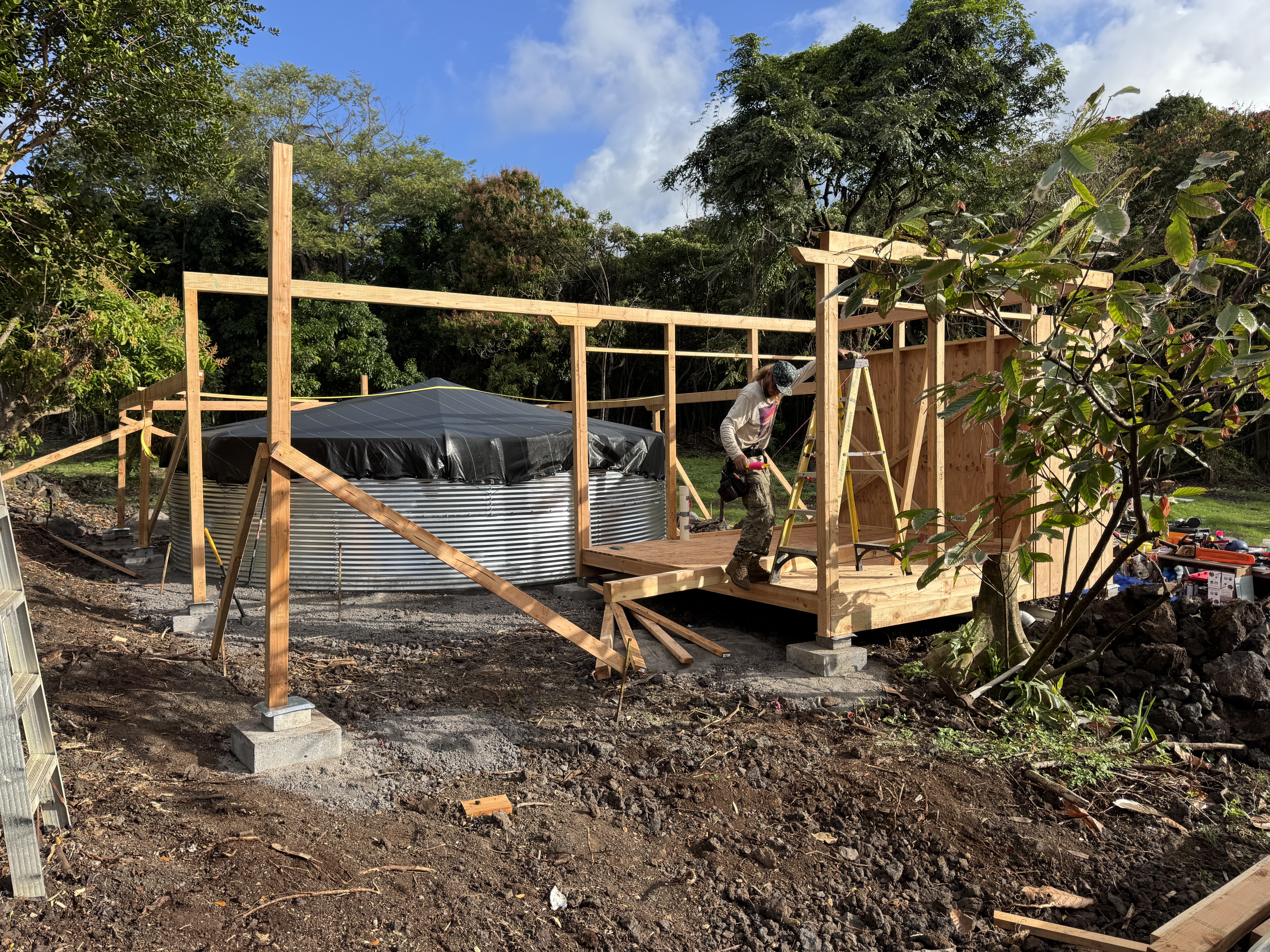 The off-grid shop and pump house with a metal roof sheltering the large galvanized rainwater catchment tank