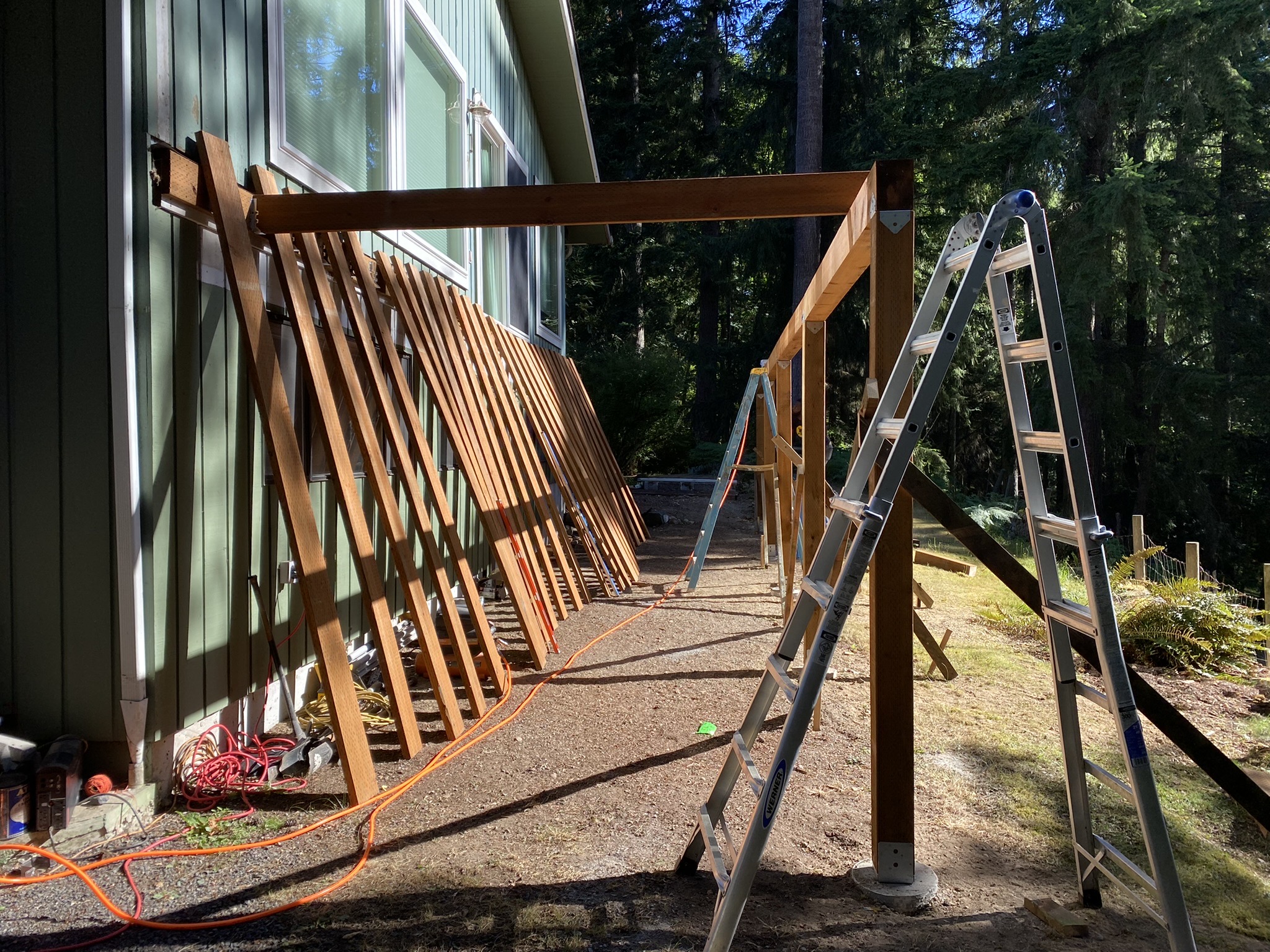 Demolition of the existing wraparound deck in progress, old decking boards leaned against the house siding as Pelletier Construction begins the rebuild