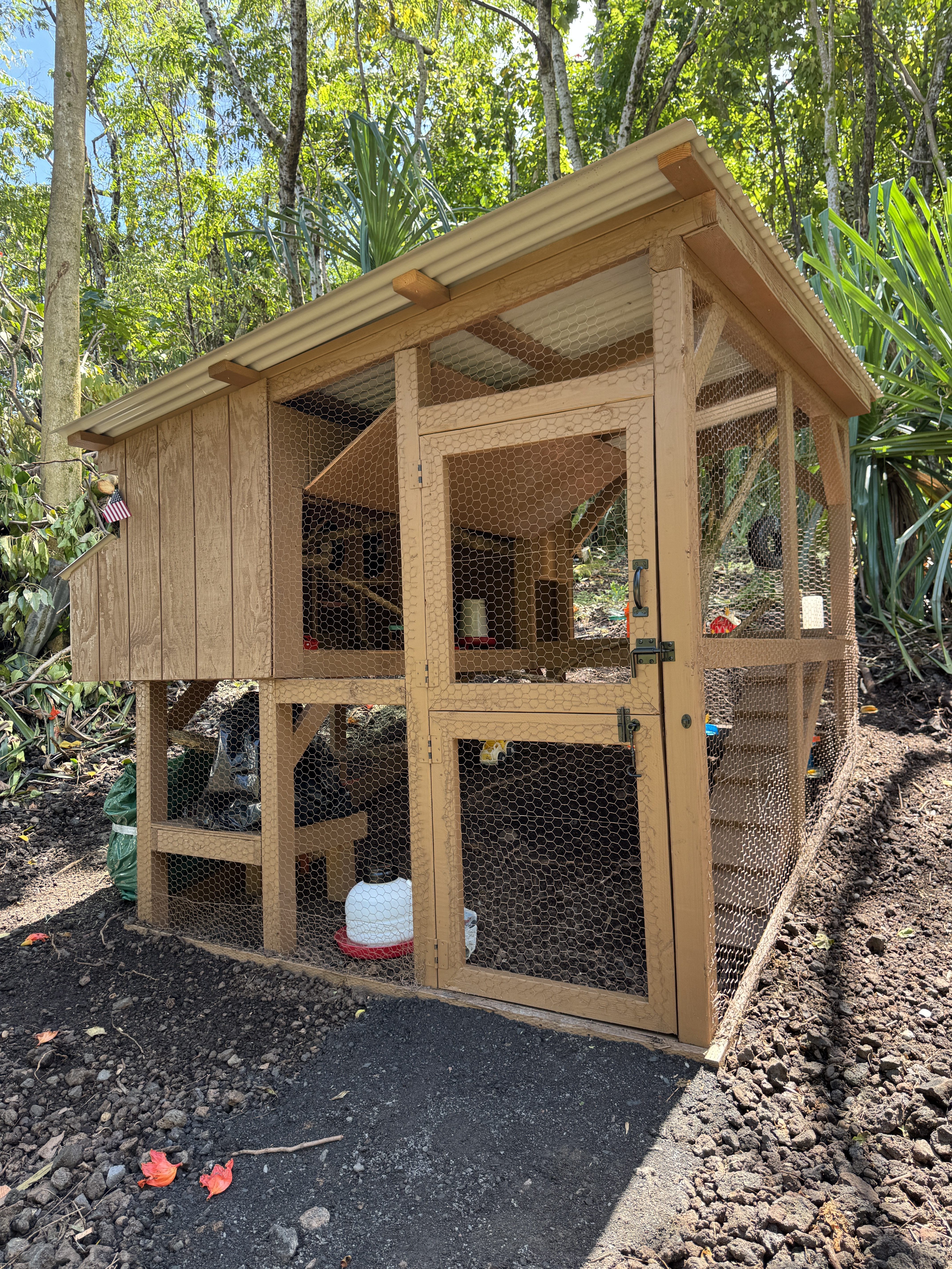 A hand-built two-story wooden chicken coop with a covered roost and a fenced run on a cinder base