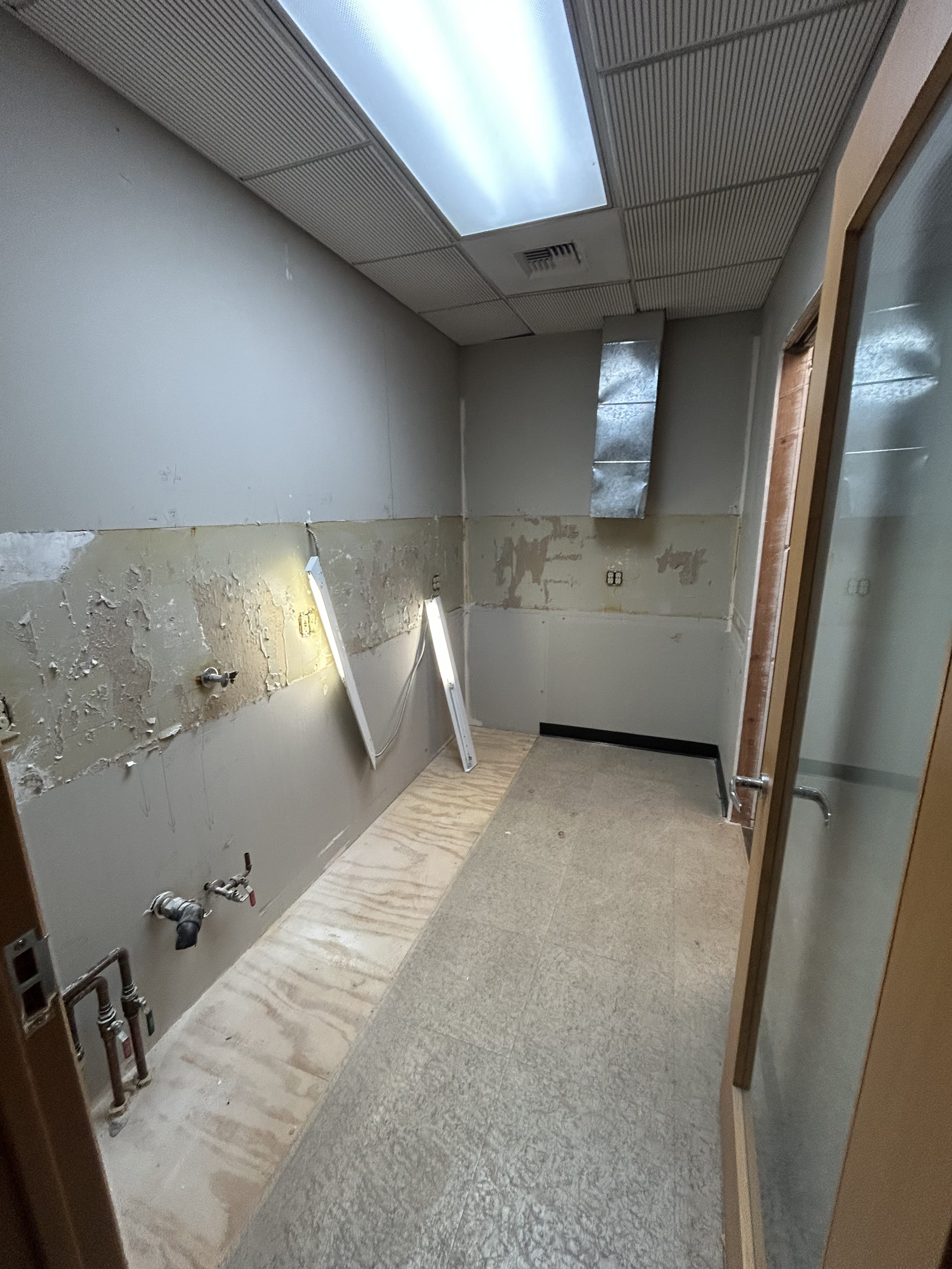 Dental lab room gutted to studs with plumbing stubs and subfloor exposed during demolition